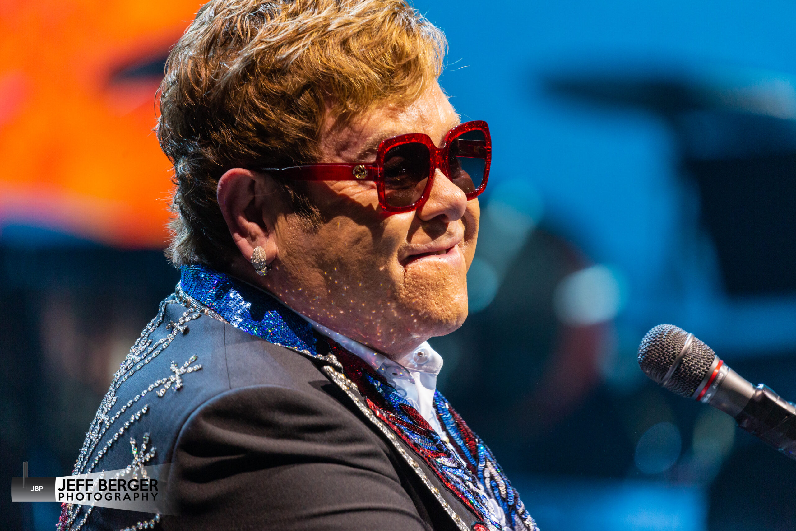 Elton John performing at the piano under warm stage lighting