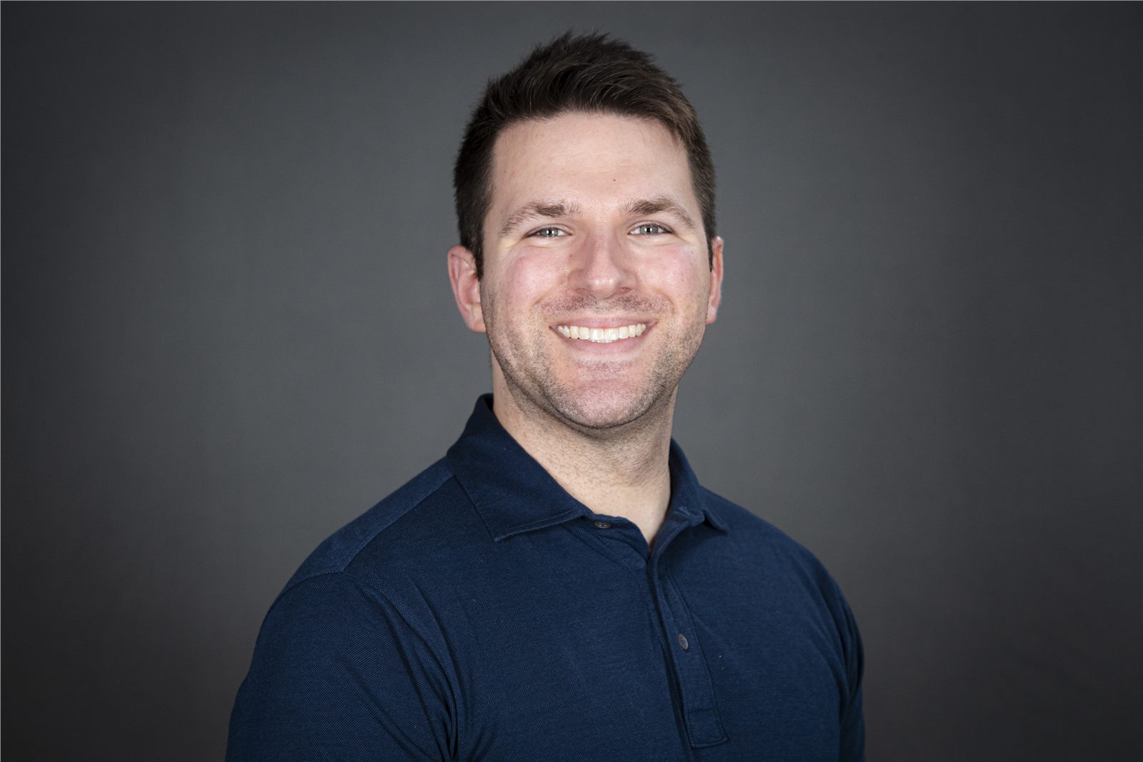 Professional headshot of a smiling man against a dark neutral background