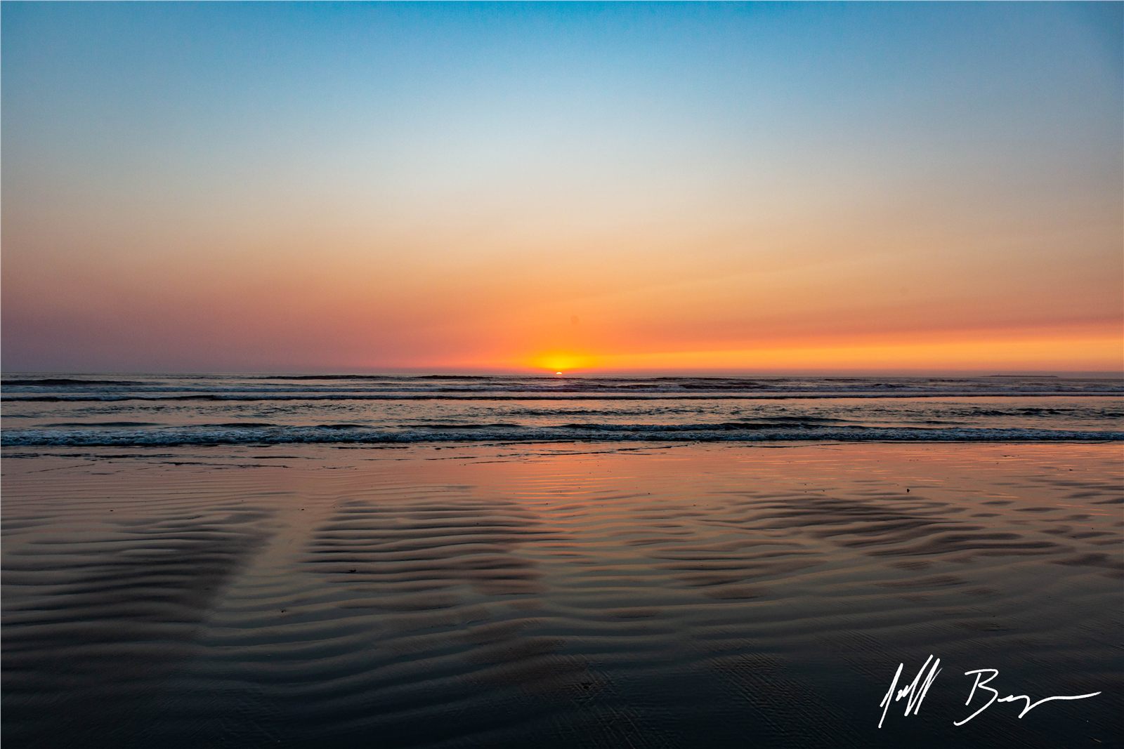 Pastel sunset over the ocean reflected in wet sand