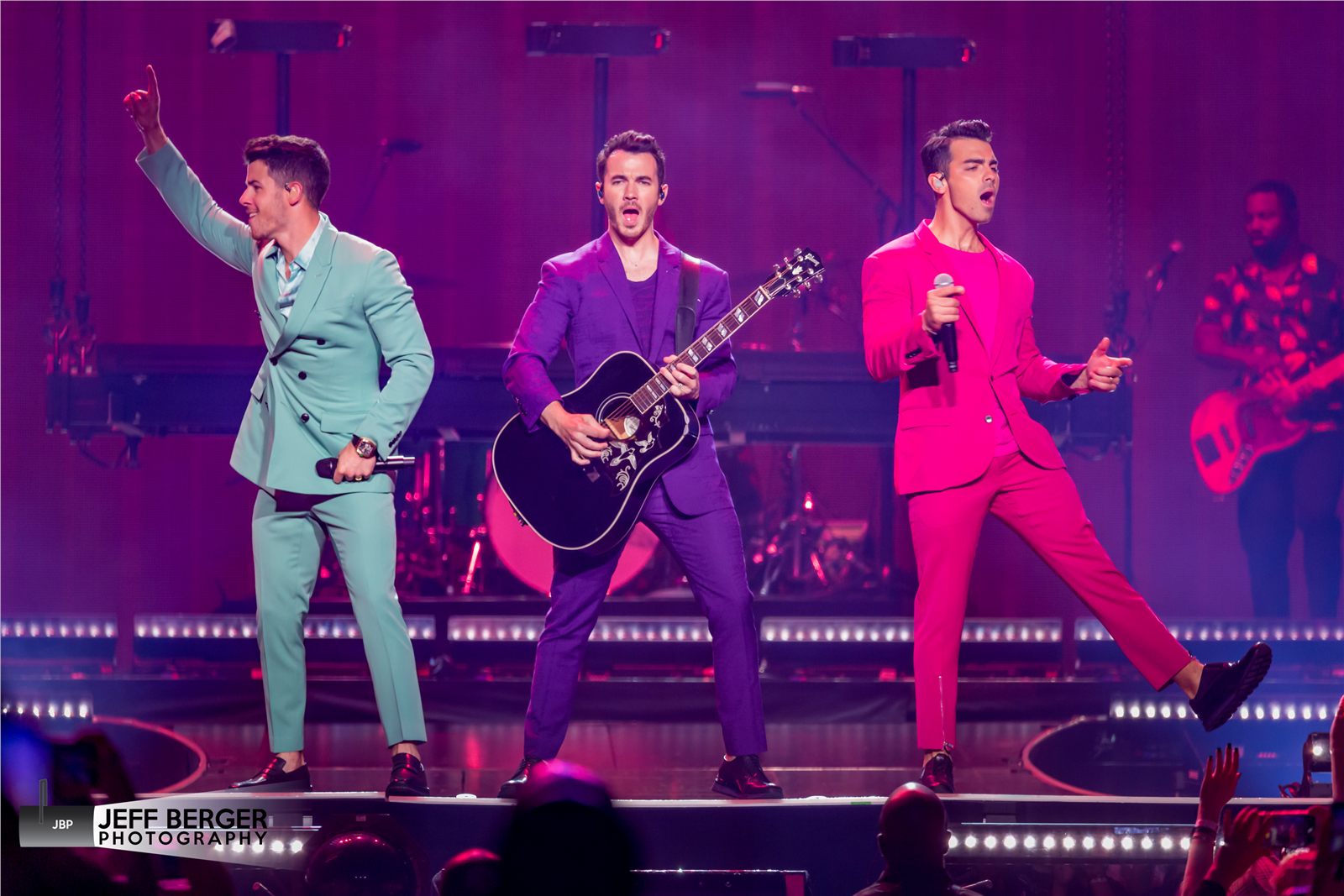 Jonas Brothers performing together under colorful stage lighting