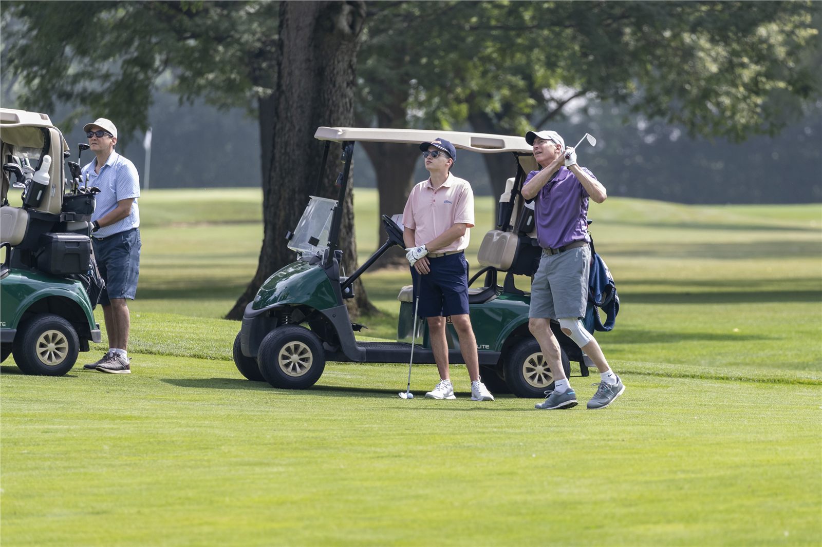 Golfers watching a shot beside carts during a group outing
